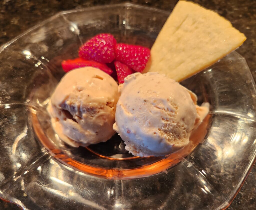 A bowl of ice cream with strawberries and a cracker.