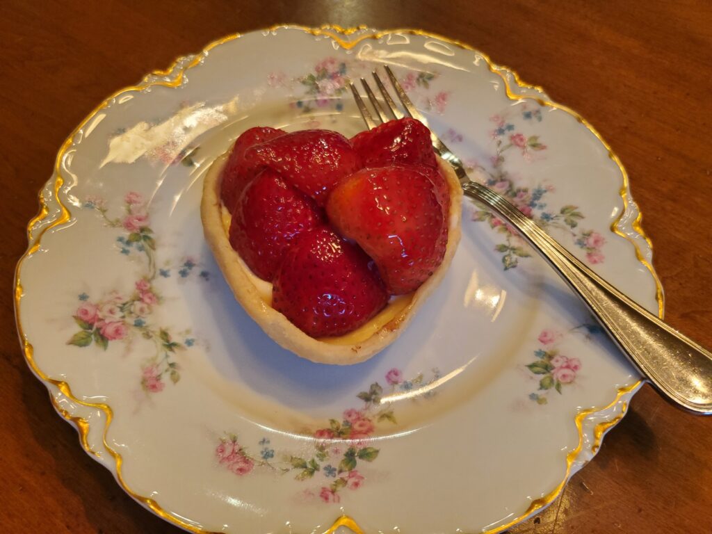 A heart shaped strawberry tart on a plate with a fork.