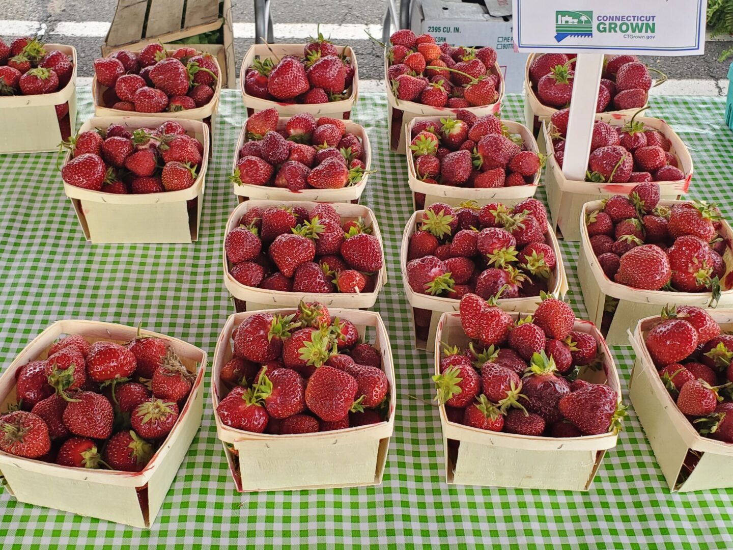 A table covered with boxes of strawberries on top of green and white checkered cloth.