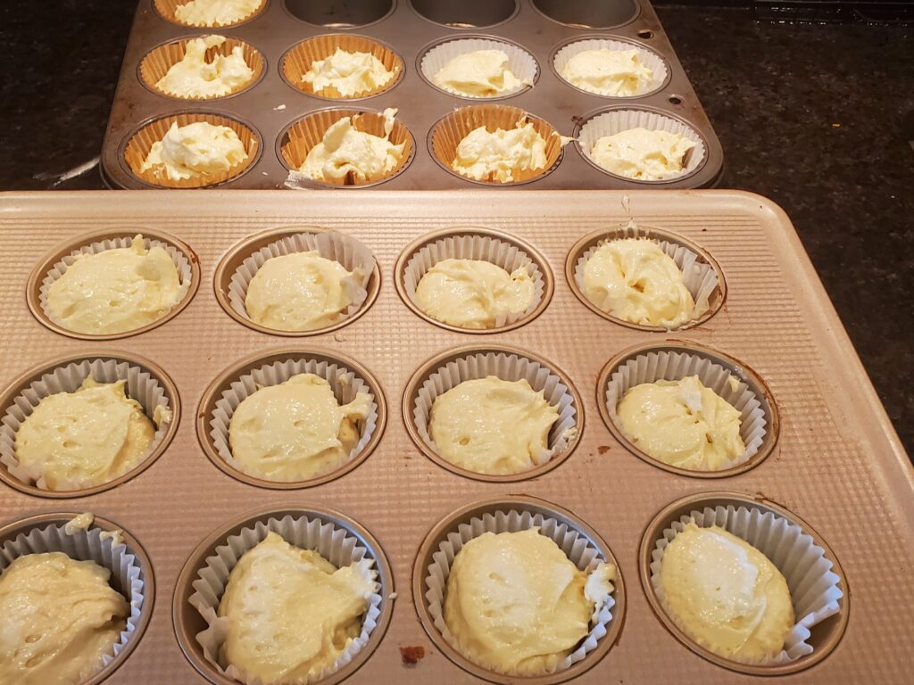 A tray of muffins with one being filled.