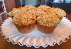 A white plate topped with muffins covered in coconut.