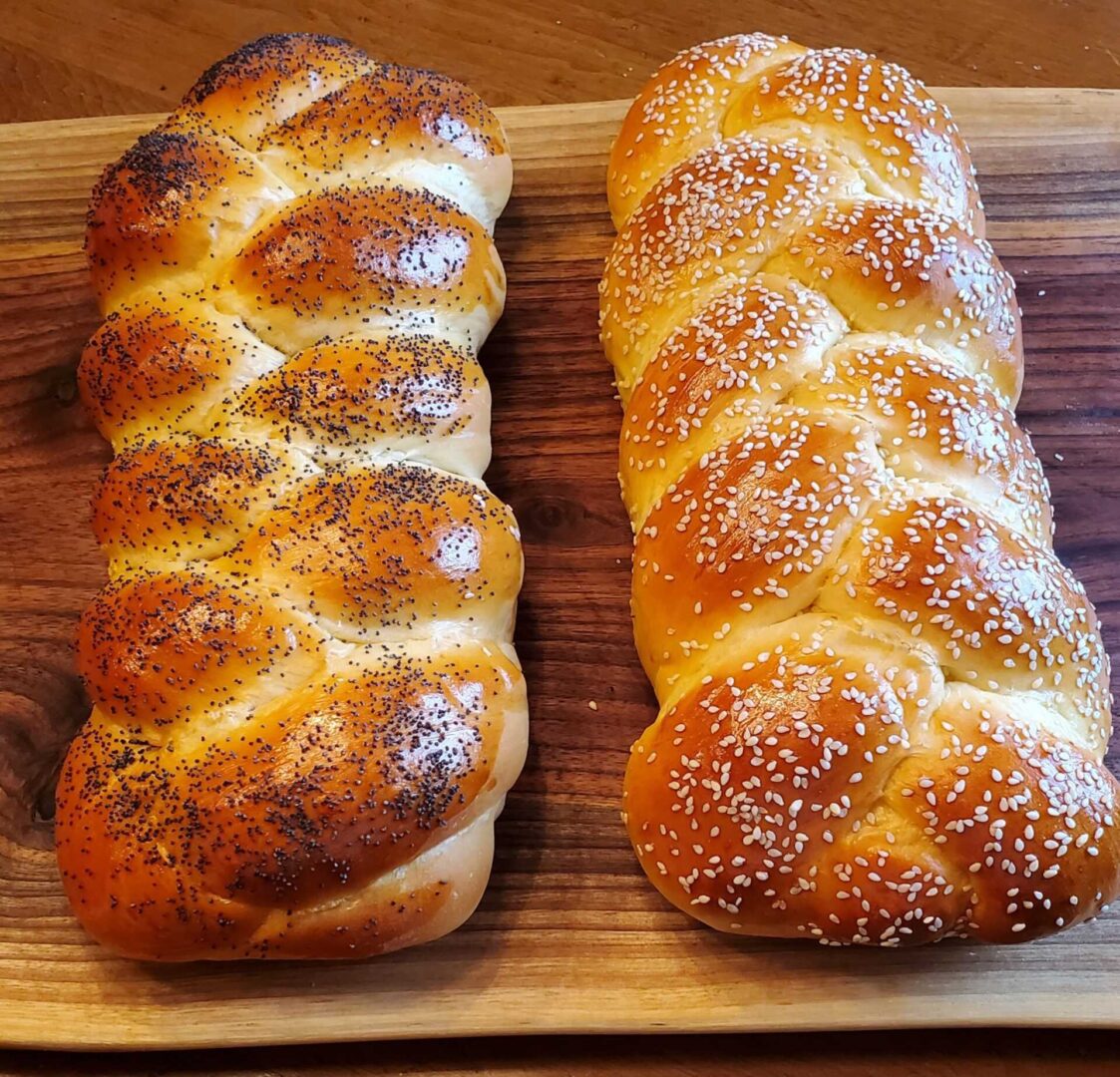The Friday Baking Project presents two braided breads on a wooden cutting board.