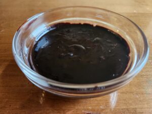 A bowl of chocolate sauce on a wooden table.