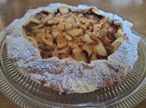 A pie with apples and powdered sugar on a plate.