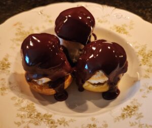 Three chocolate covered pastries on a plate.