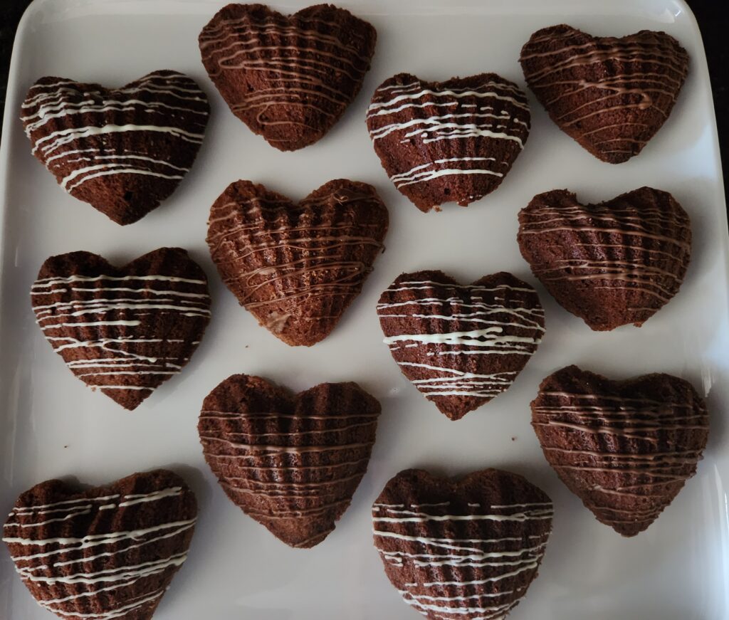 A tray of heart-shaped chocolate cookies decorated with white icing.