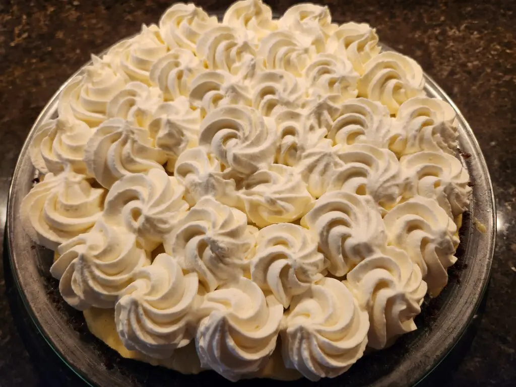 A pie topped with swirls of whipped cream on a glass plate.