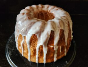 A freshly baked bundt cake with white glaze on a glass serving plate.