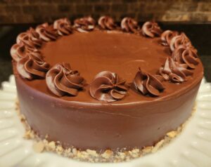 A chocolate cake topped with swirls of chocolate frosting, presented on a white plate.