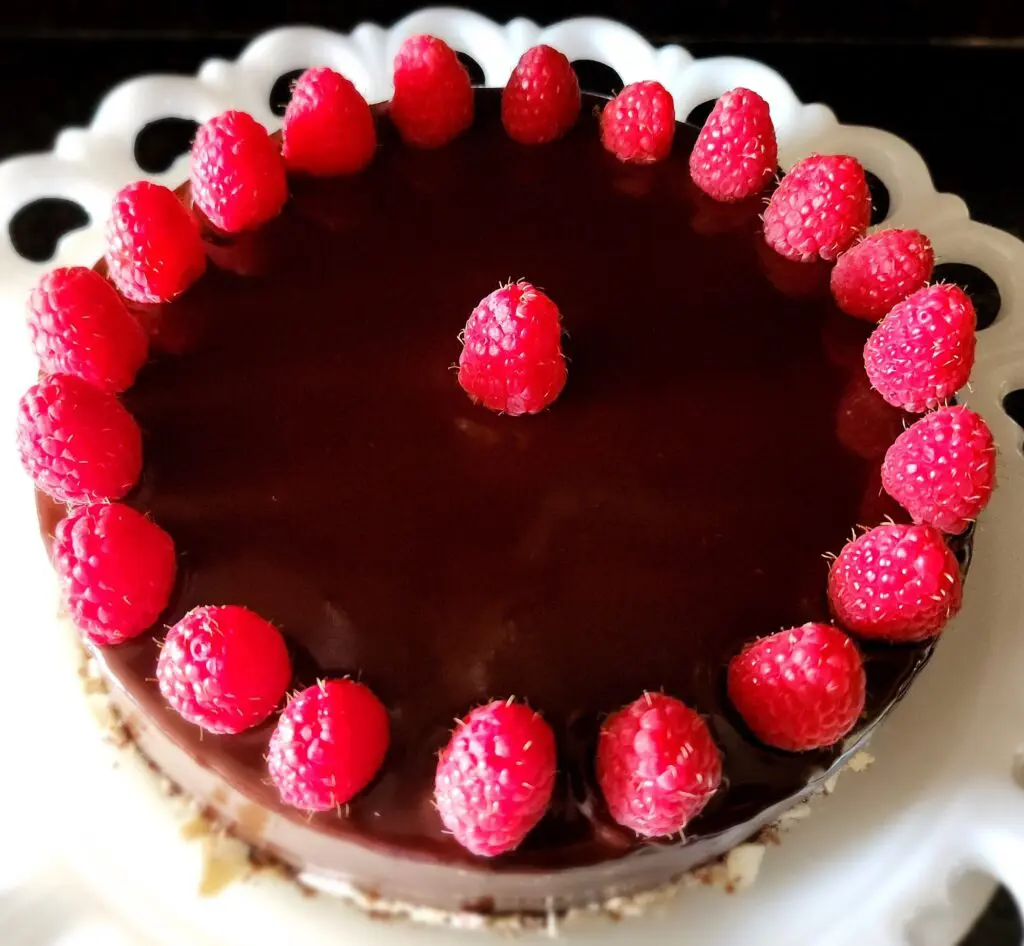 A chocolate ganache cake topped with fresh raspberries arranged in a circular pattern on a white plate.