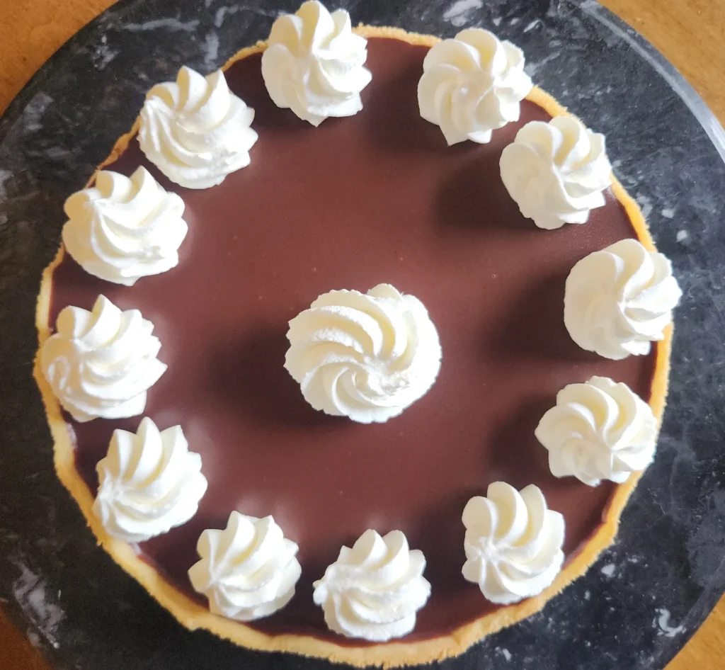 Chocolate cake topped with evenly spaced whipped cream swirls.